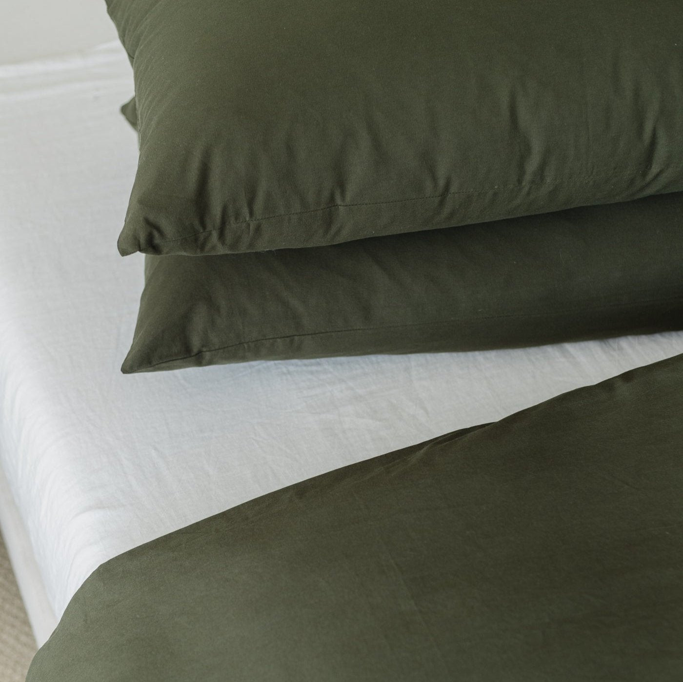 Olive green duvet cover with matching pillowcases and white insert on bed.