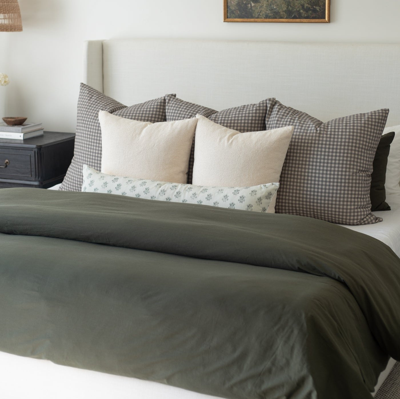 Olive green duvet cover on king bed with gingham and solid decorative pillows.