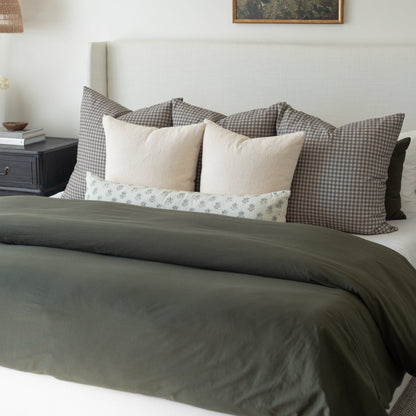 Olive green duvet cover on king bed with gingham and solid decorative pillows.