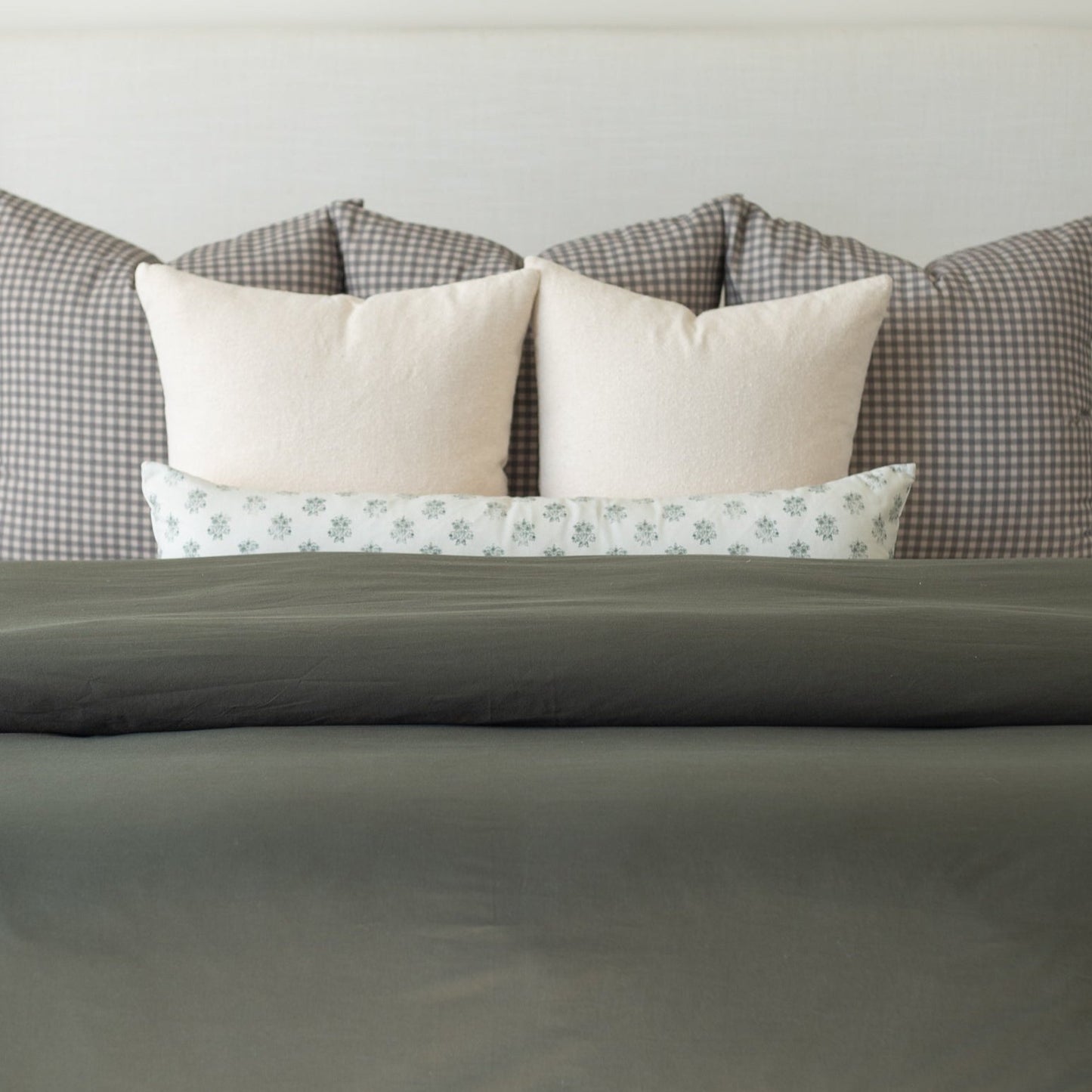 Olive green duvet cover on bed with cream and patterned pillows displayed against headboard.