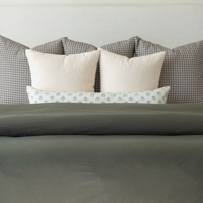 Olive green duvet cover on bed with cream and patterned pillows displayed against headboard.