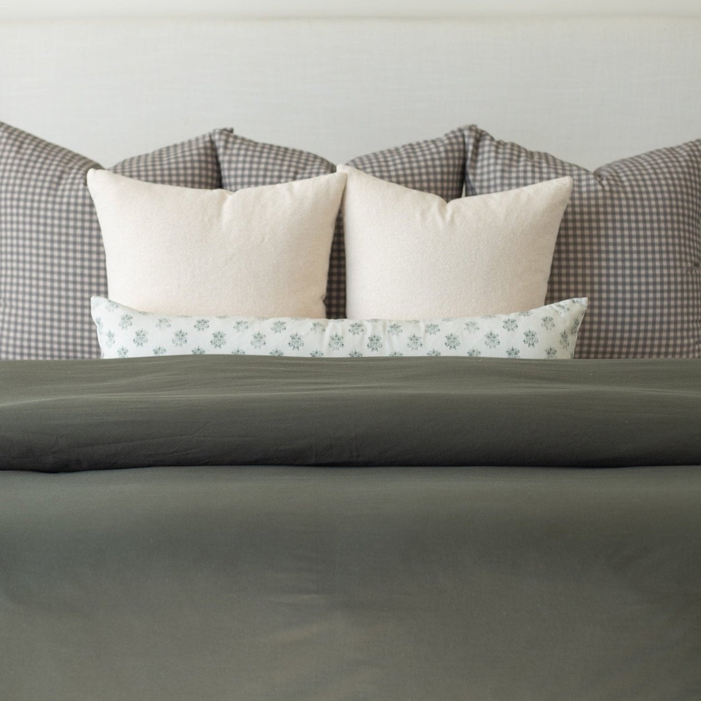 Olive duvet cover on bed with cream pillows and patterned pillows behind it.