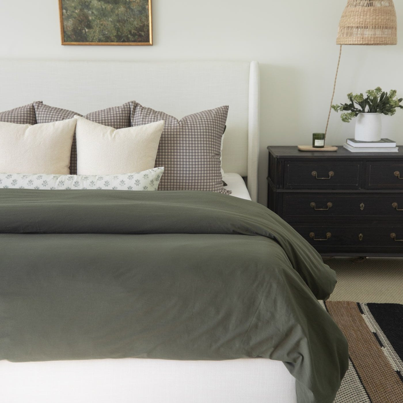 Olive green duvet cover on king bed with gingham pillows and cream shams.