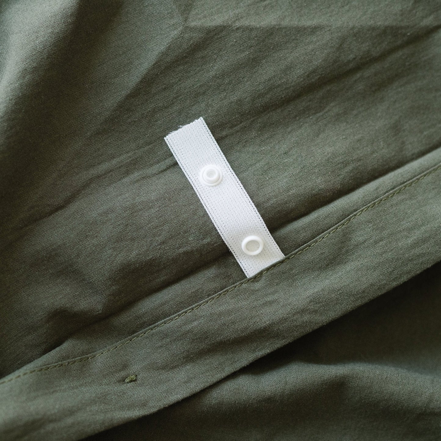 Olive-colored duvet cover with white button closure strip on gathered fabric.