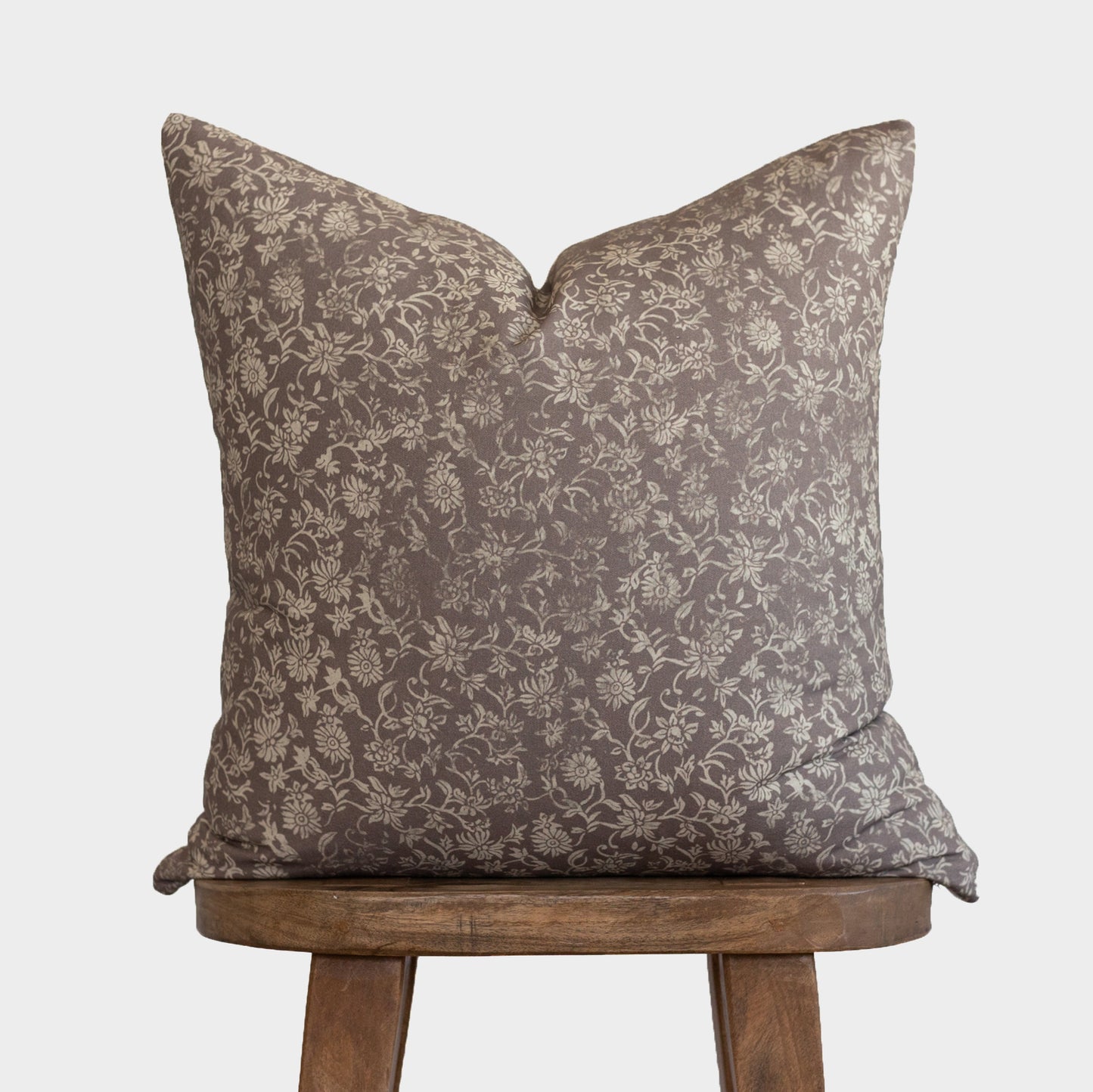Taupe floral patterned pillow with cream botanical design, displayed on wooden chair legs.