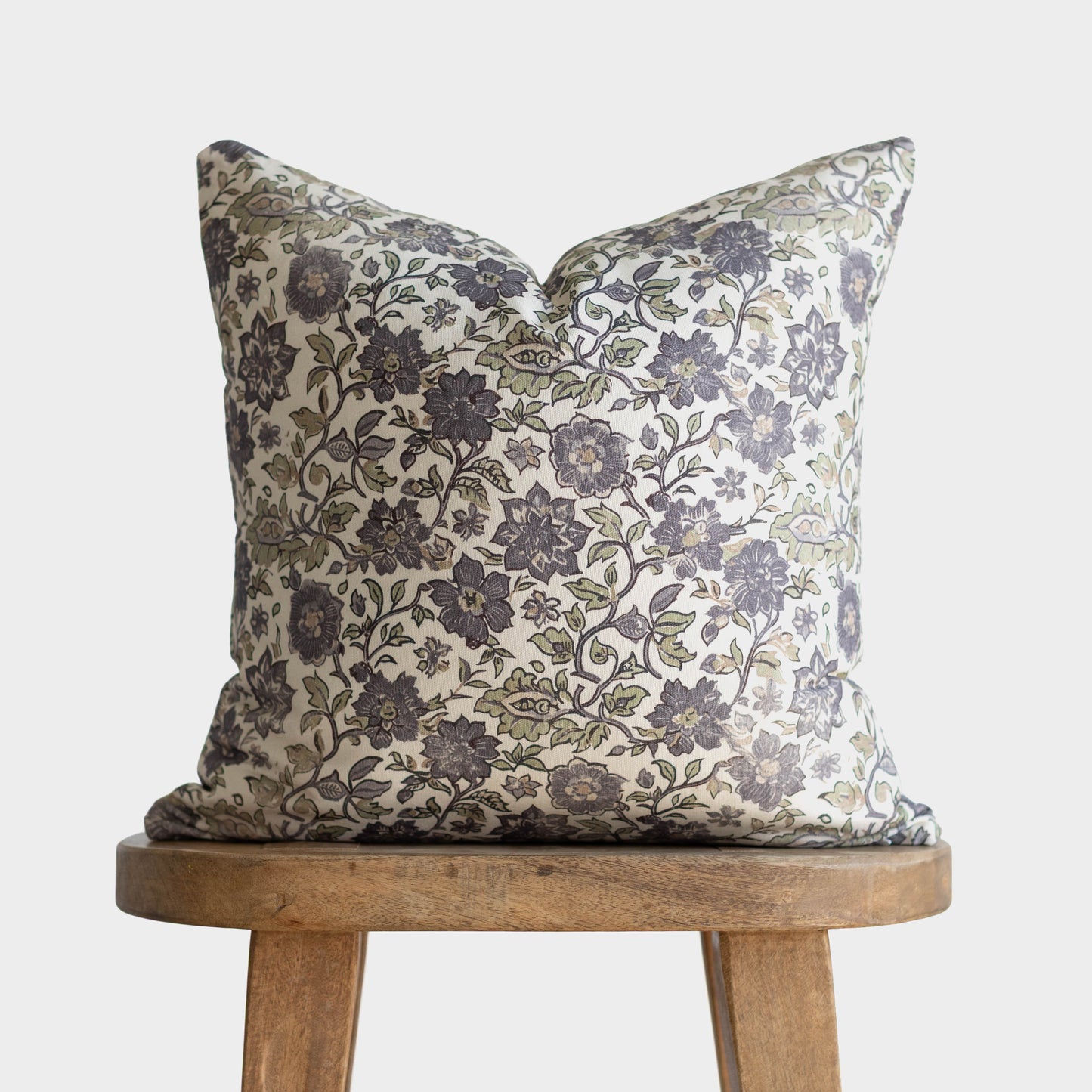 Square pillow with cream and navy floral damask pattern on wooden stool.