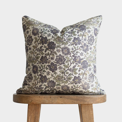 Square pillow with cream and navy floral damask pattern on wooden stool.