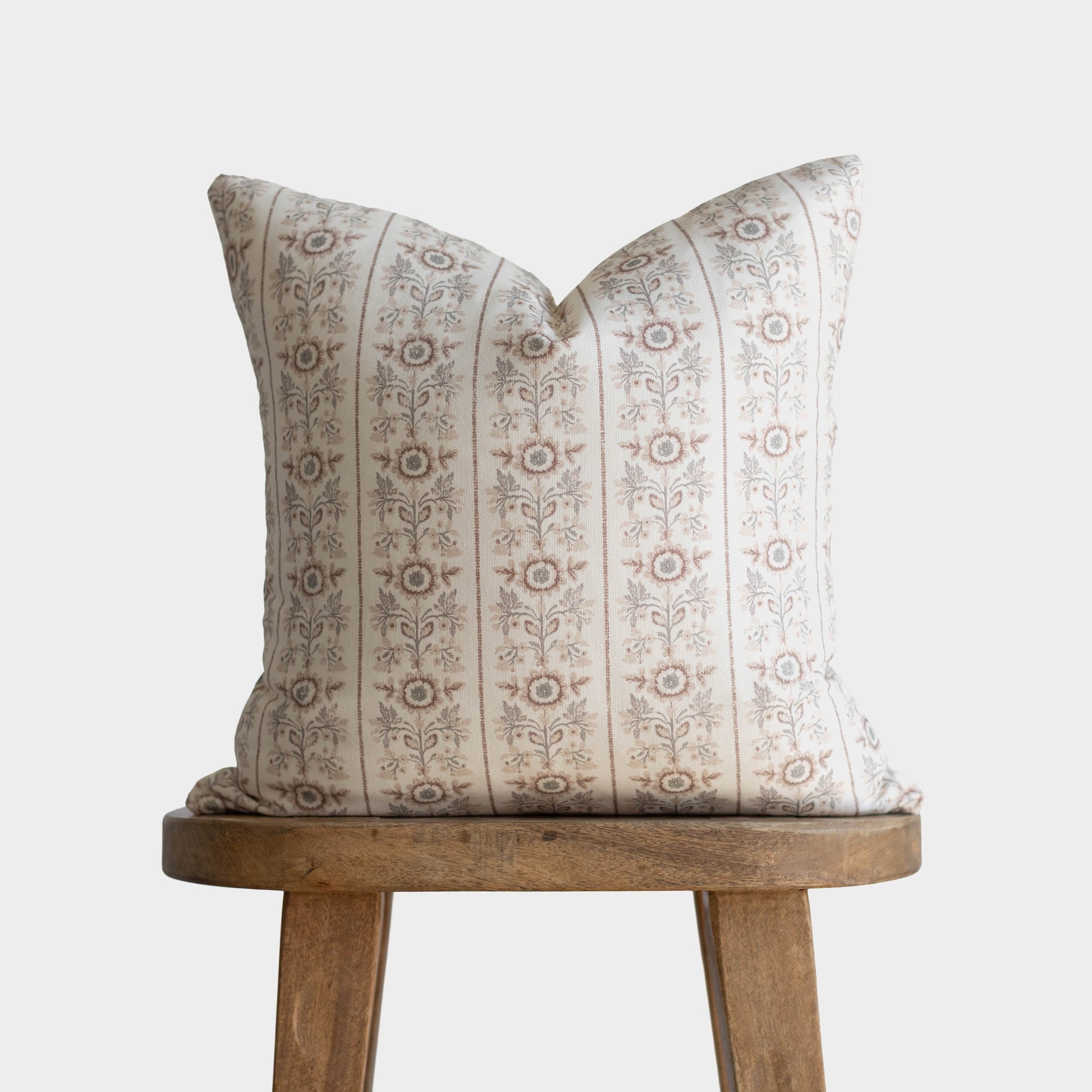Cream pillow with tan floral stripe pattern displayed on wooden stool.