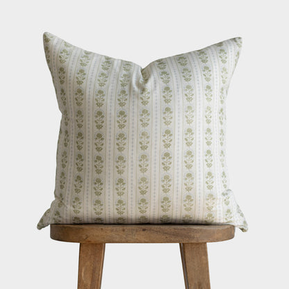 Square throw pillow with sage green floral stripe pattern on cream linen displayed on wooden stool.