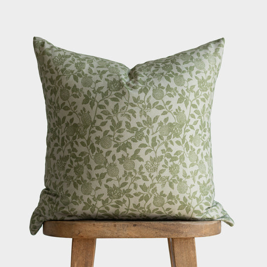 Green and cream botanical patterned throw pillow with leafy vine design, displayed on wooden stool.
