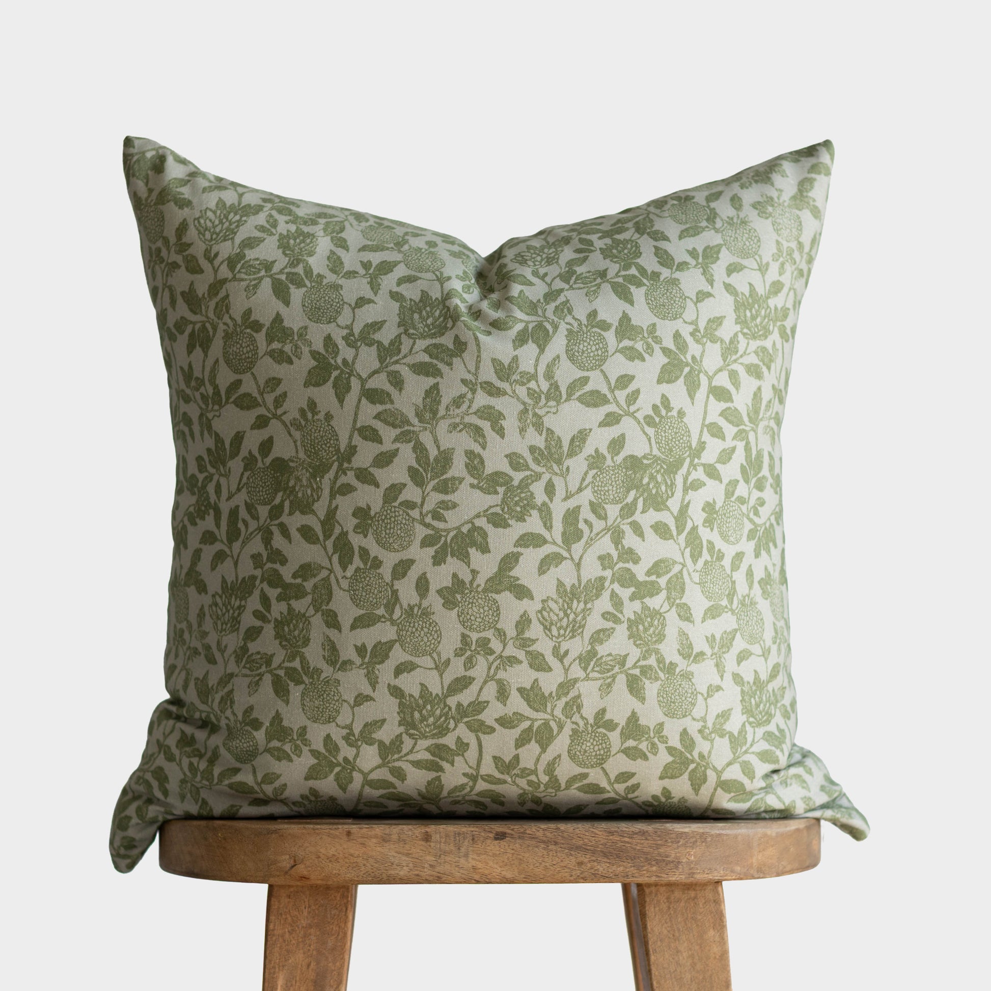 Green and cream floral patterned pillow cover with leaf and berry design displayed on wooden stool.