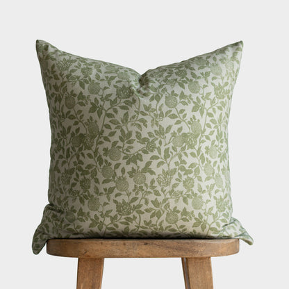 Green and cream floral patterned pillow cover with leaf and berry design displayed on wooden stool.