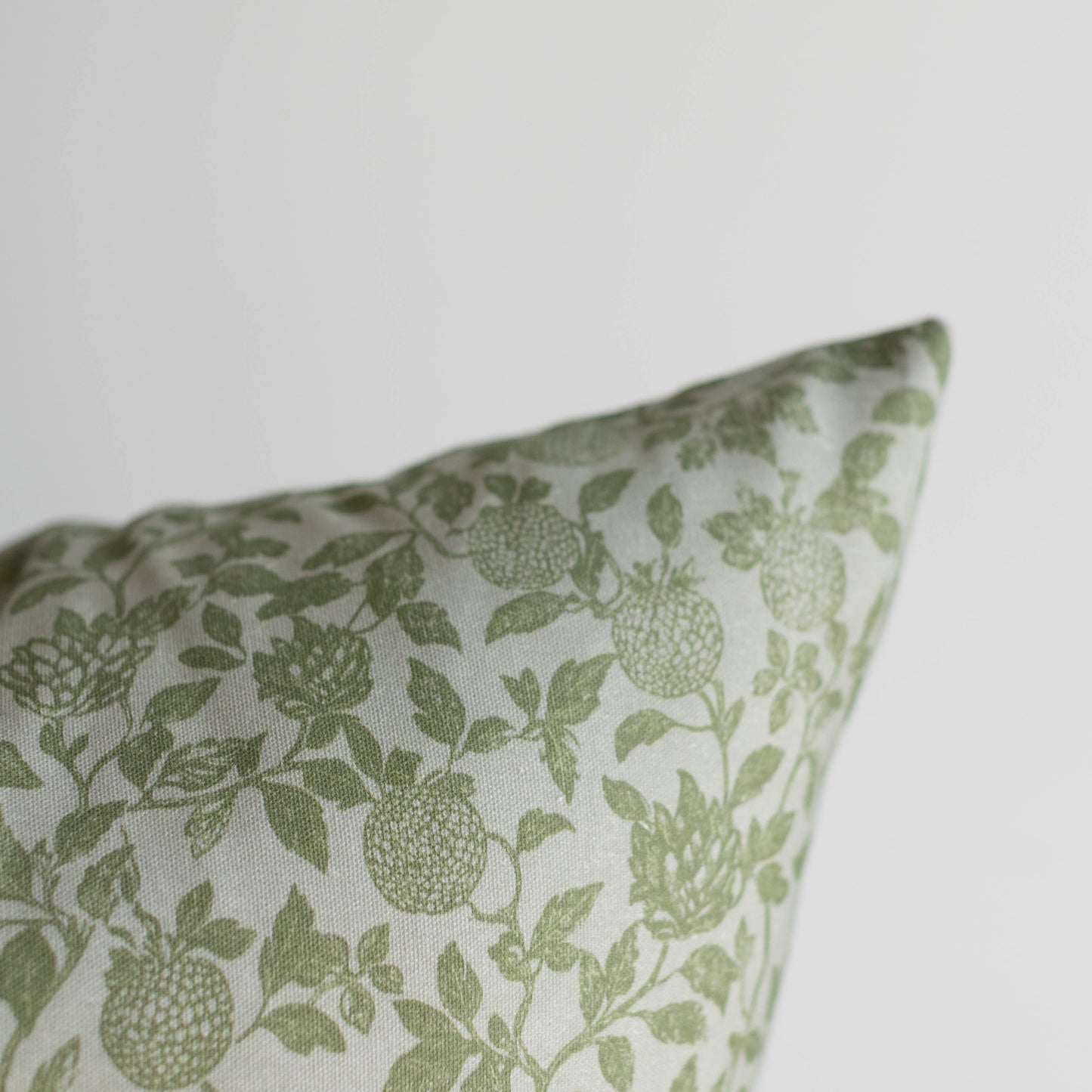 Green and white pillow with botanical print featuring fruits and leafy stems.