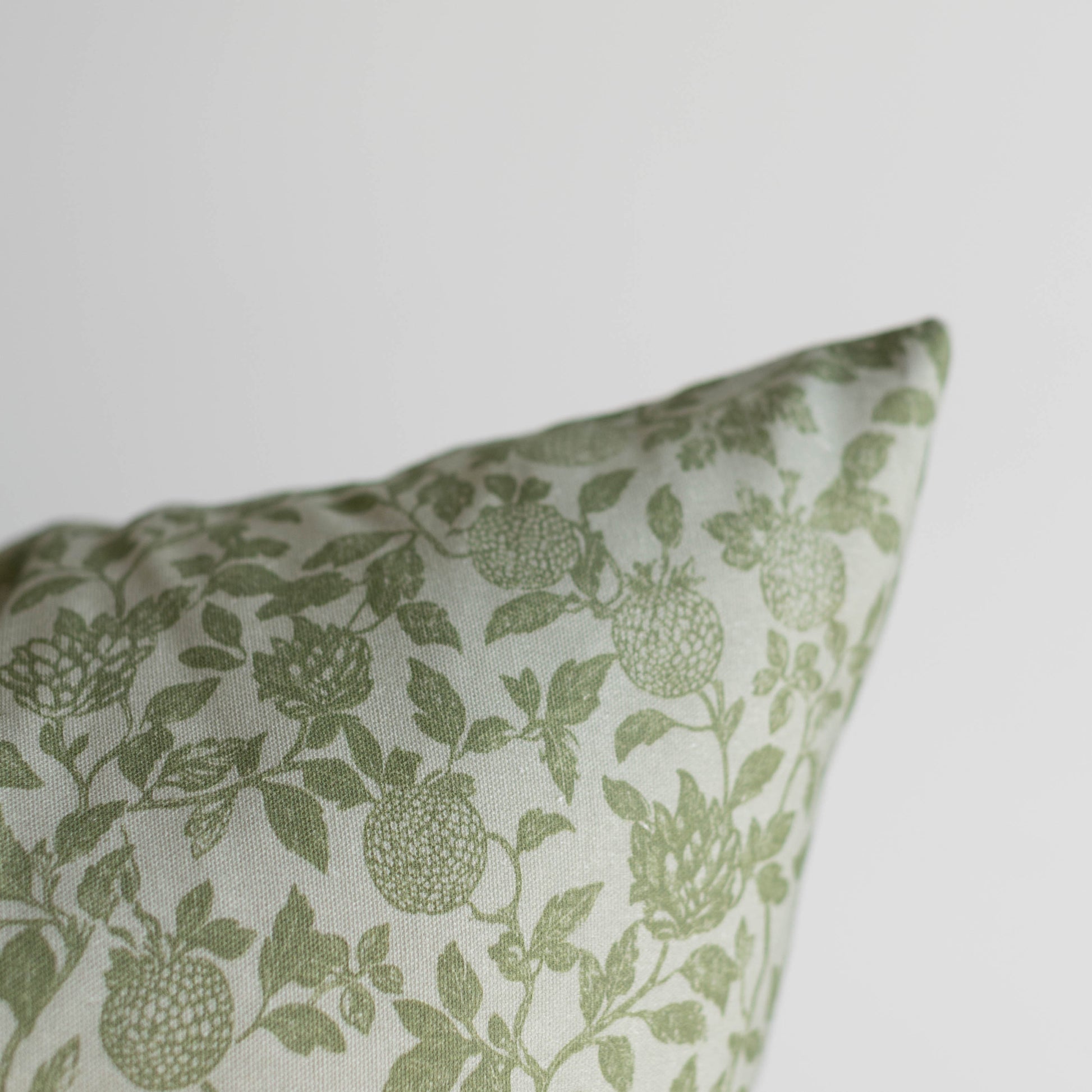 Green and white pillow with botanical print featuring fruits and leafy stems.