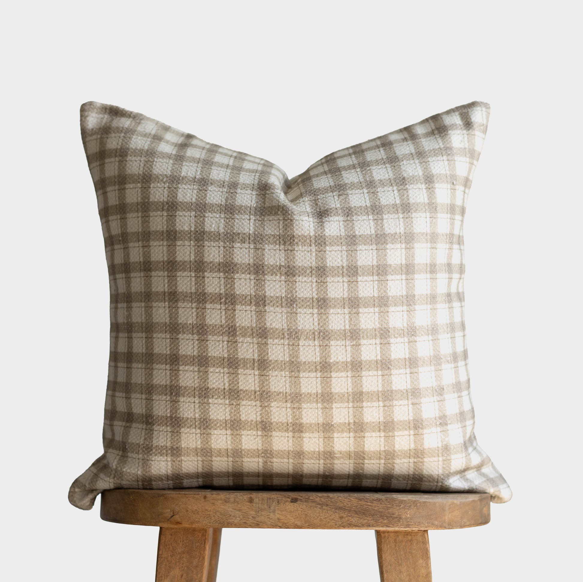 Beige and white gingham plaid cotton pillow cover displayed on wooden stool.