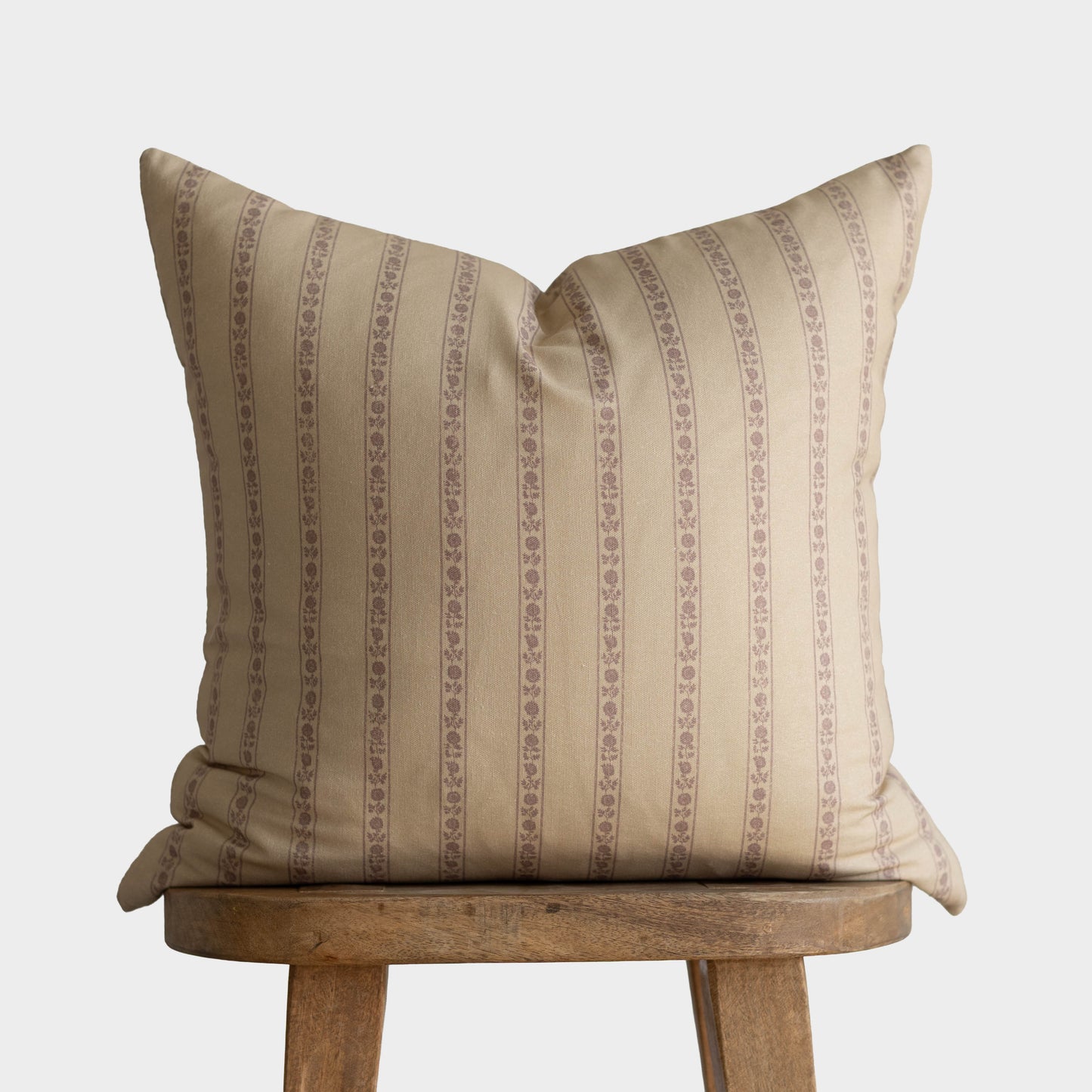 Cream pillow with tan vertical stripe and floral pattern detail, displayed on wooden stool.