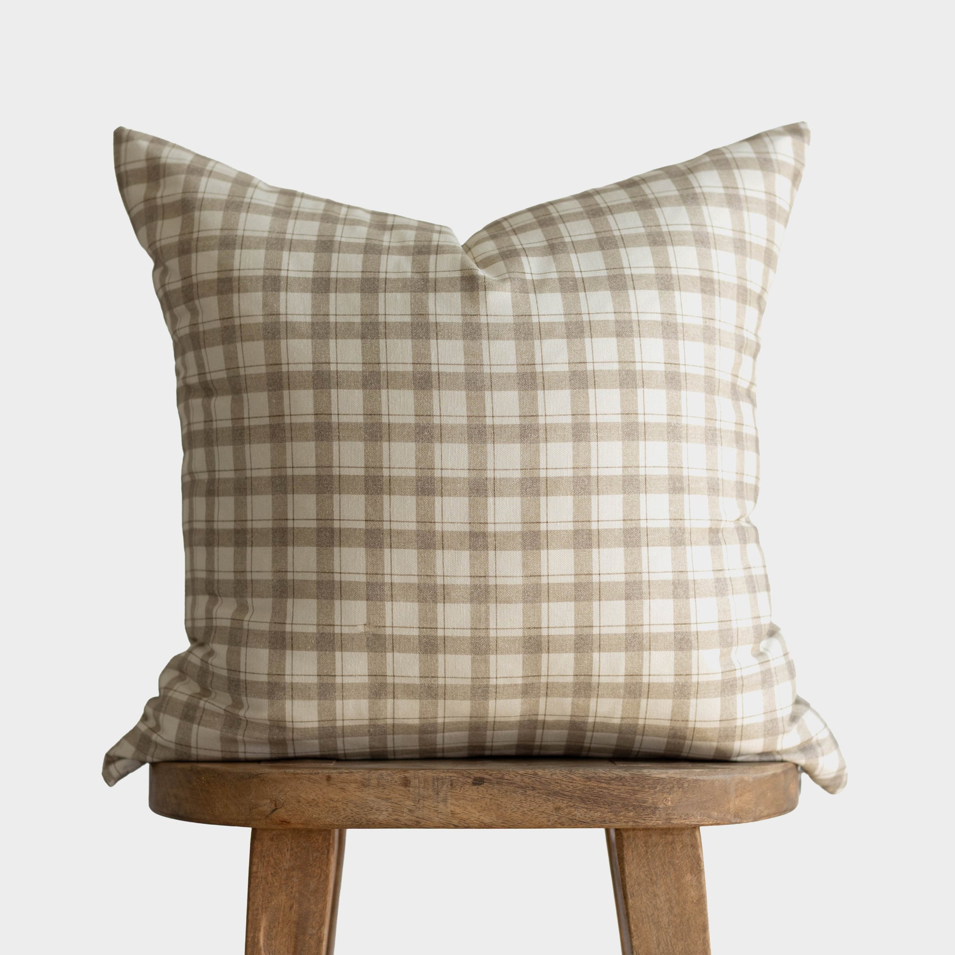 Beige and cream plaid pillow cover on wooden stool against gray background.