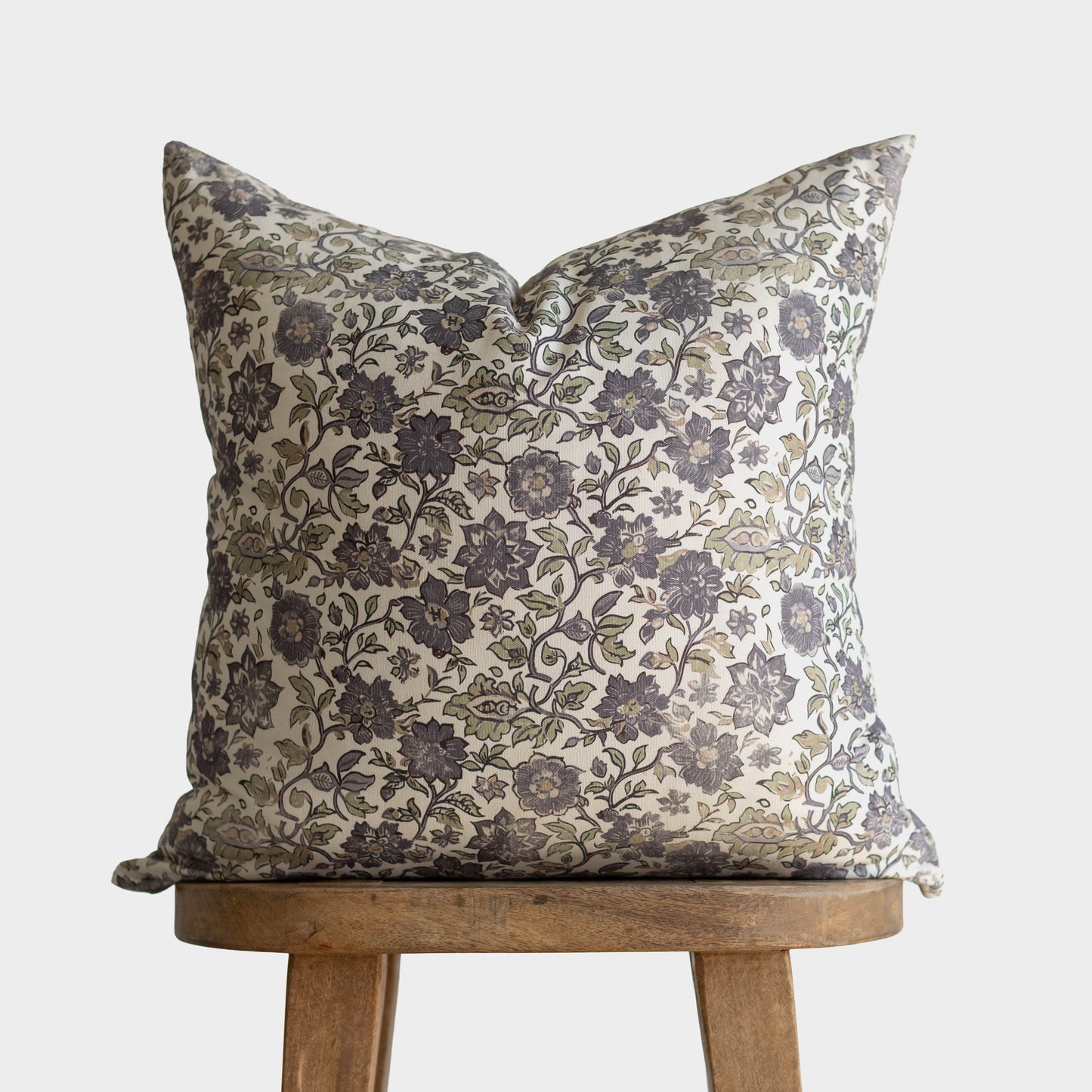 Cream pillow with dark gray floral and botanical pattern, displayed on wooden stool.