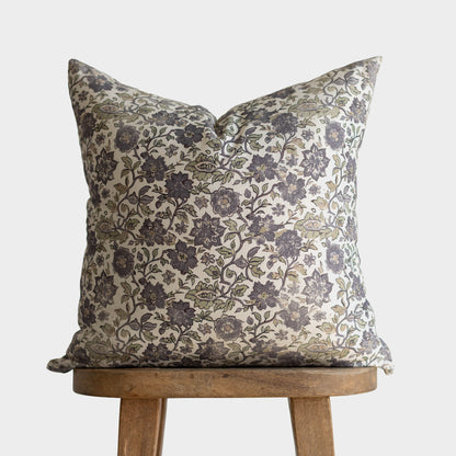 Cream pillow with dark gray floral and botanical pattern, displayed on wooden stool.