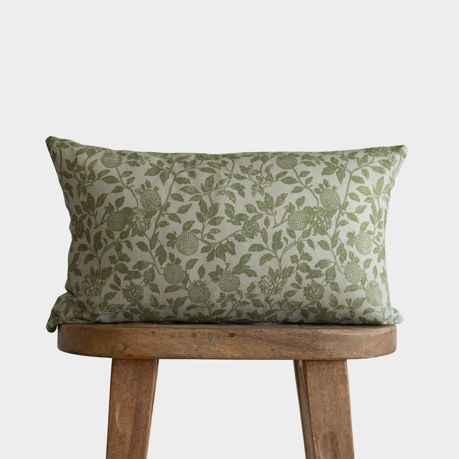 Green and cream botanical patterned double-sided pillow with leaf and fruit motifs on wooden stool.