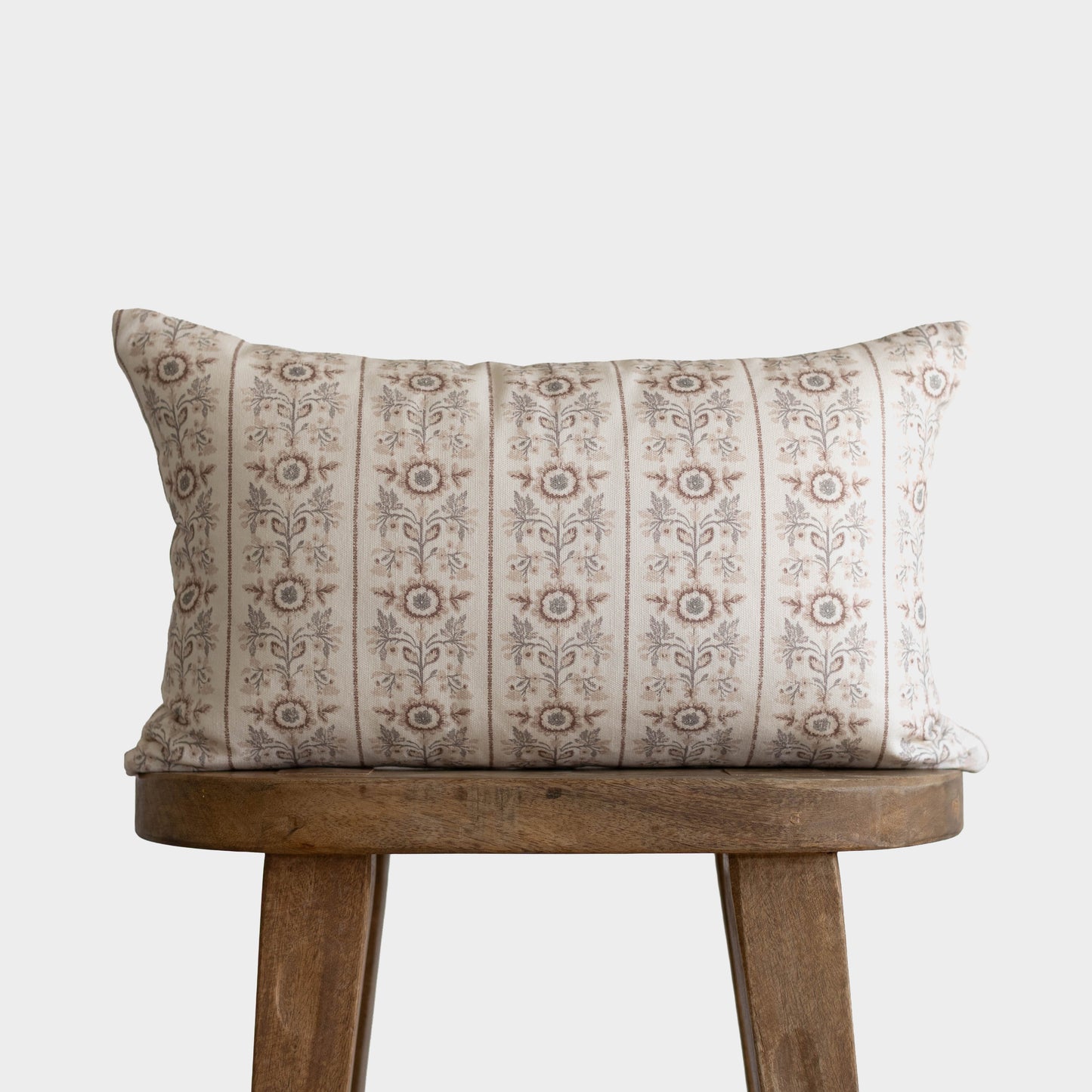 Cream and taupe striped throw pillow with floral botanical pattern, displayed on wooden stool.