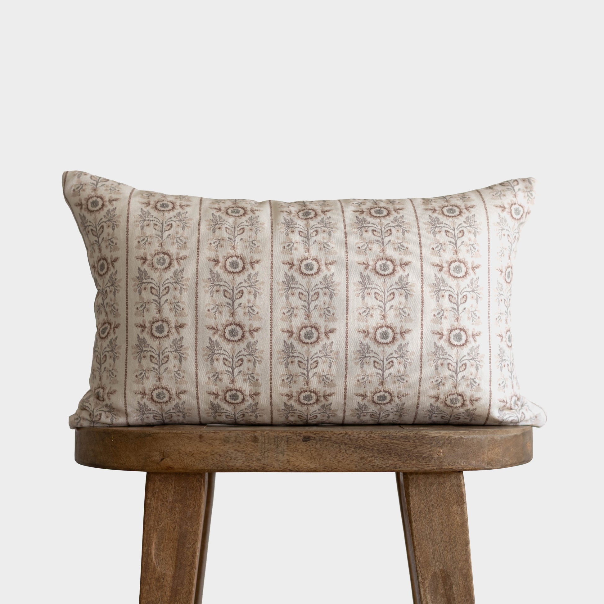 Cream and taupe striped throw pillow with floral botanical pattern, displayed on wooden stool.
