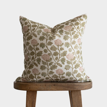 Cream pillow with green and blush floral botanical print featuring flowering branches, displayed on wooden stool.