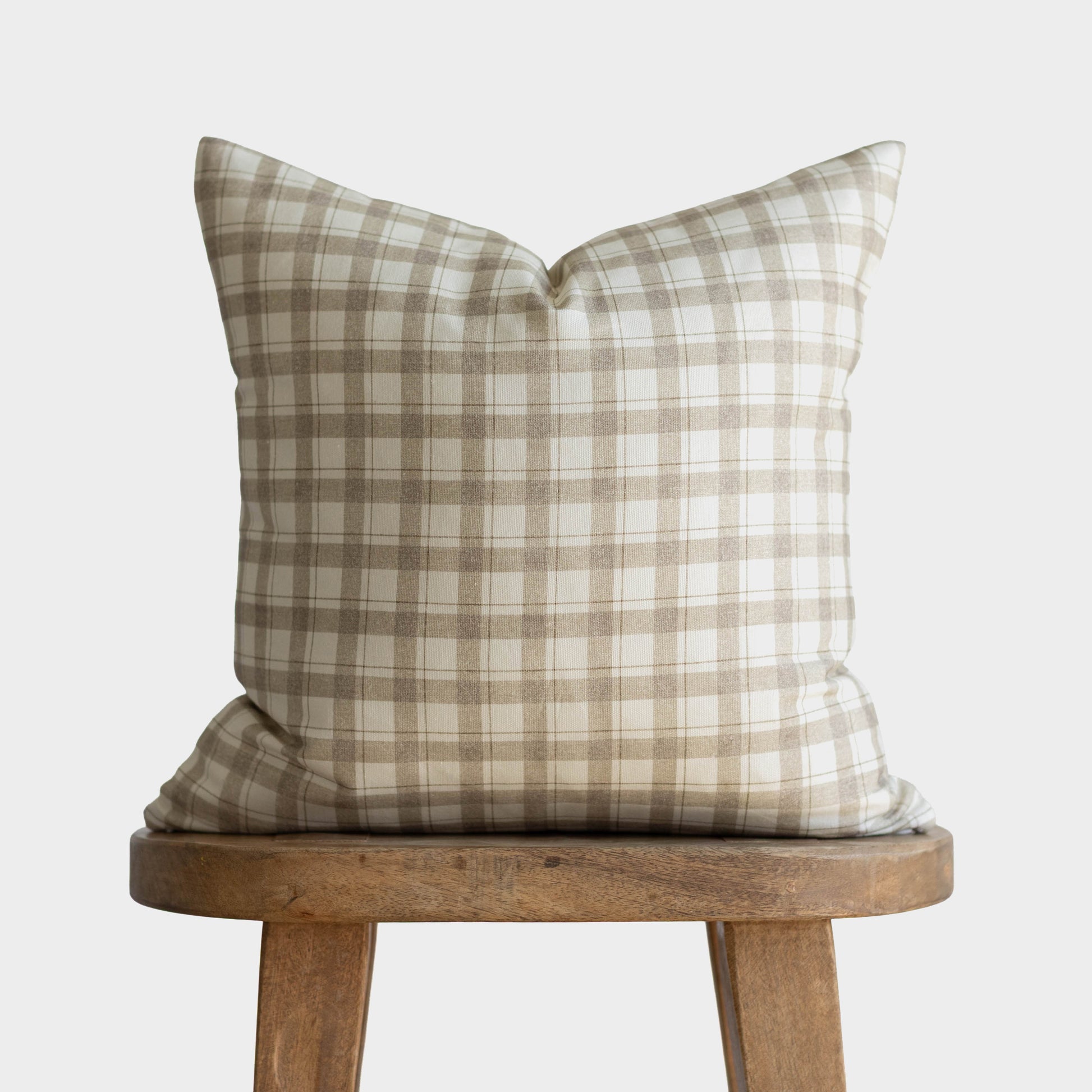 Beige and cream plaid pillow cover displayed on wooden stool.