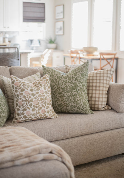 Five decorative throw pillows with floral and checkered patterns arranged on a beige sofa in a bright living room.