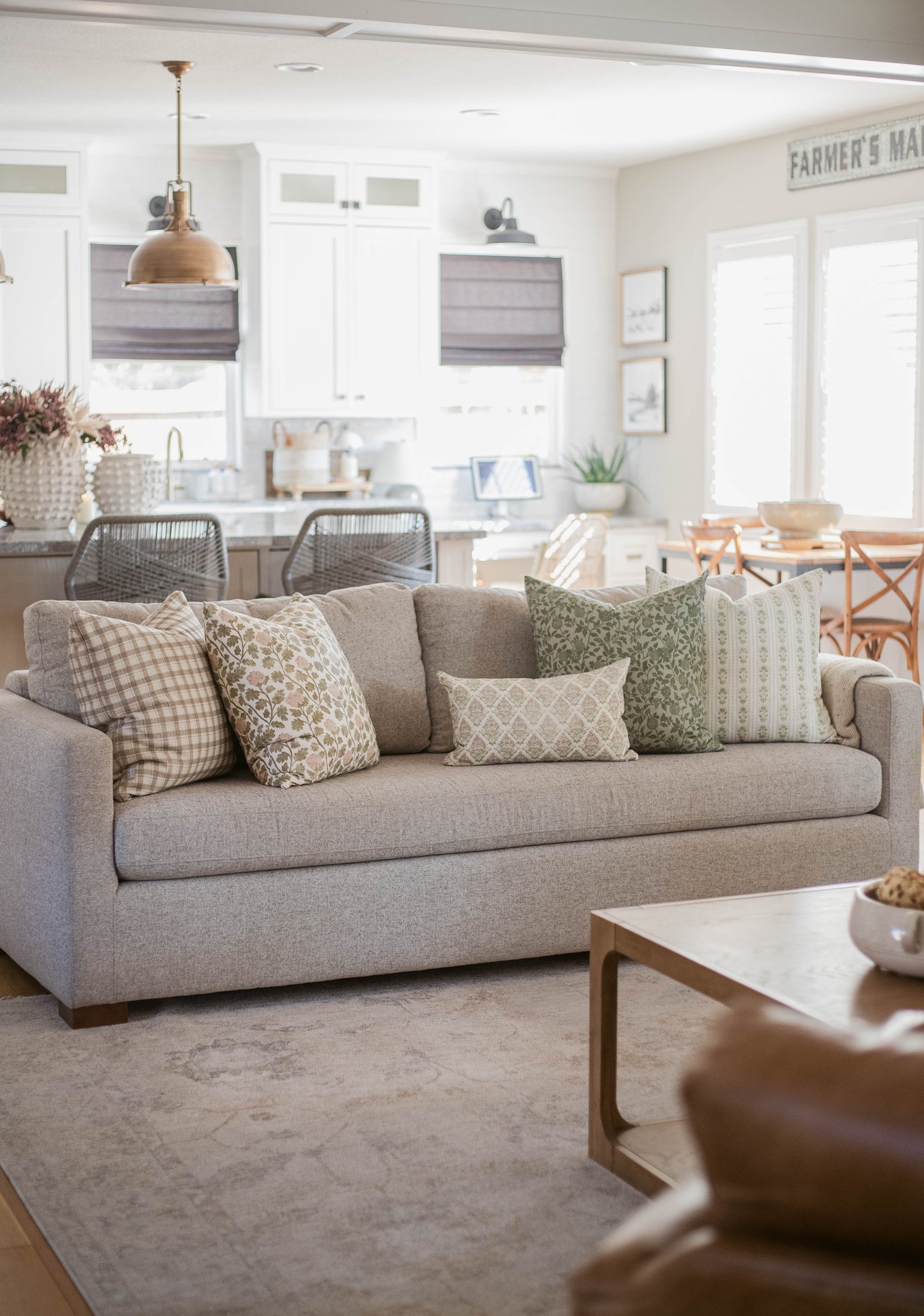 Five decorative pillows with various patterns displayed on a beige upholstered sofa in a living room.