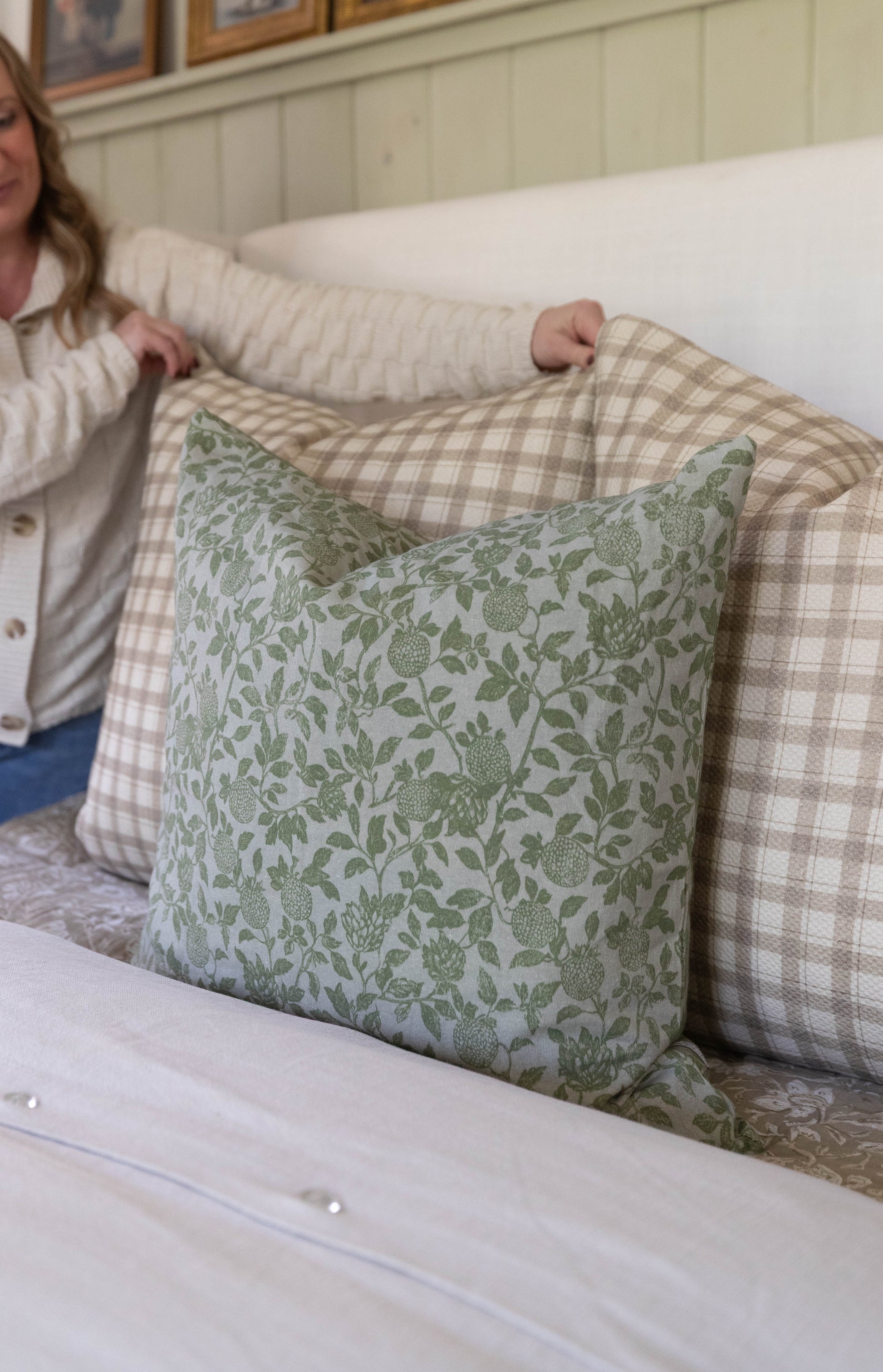 Green and cream botanical print pillow with leaves and berries displayed on a checkered upholstered bed.