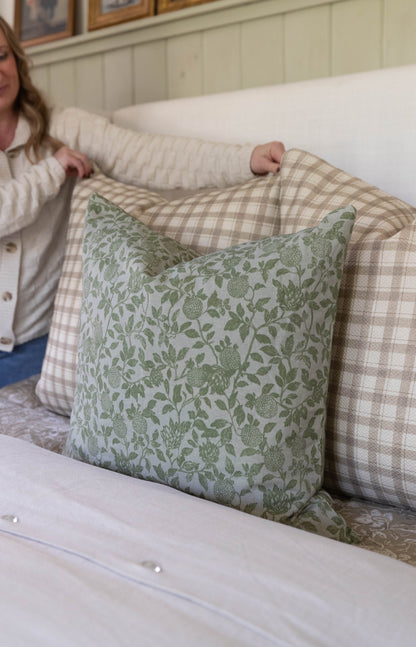 Green and cream botanical print pillow with leaves and berries displayed on a checkered upholstered bed.
