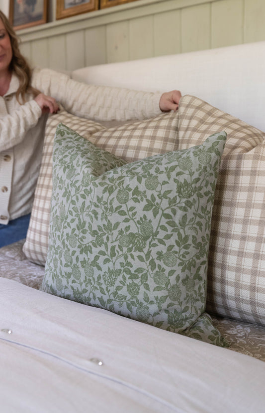 Green and cream botanical print pillow with leaves and berries displayed on a checkered upholstered bed.