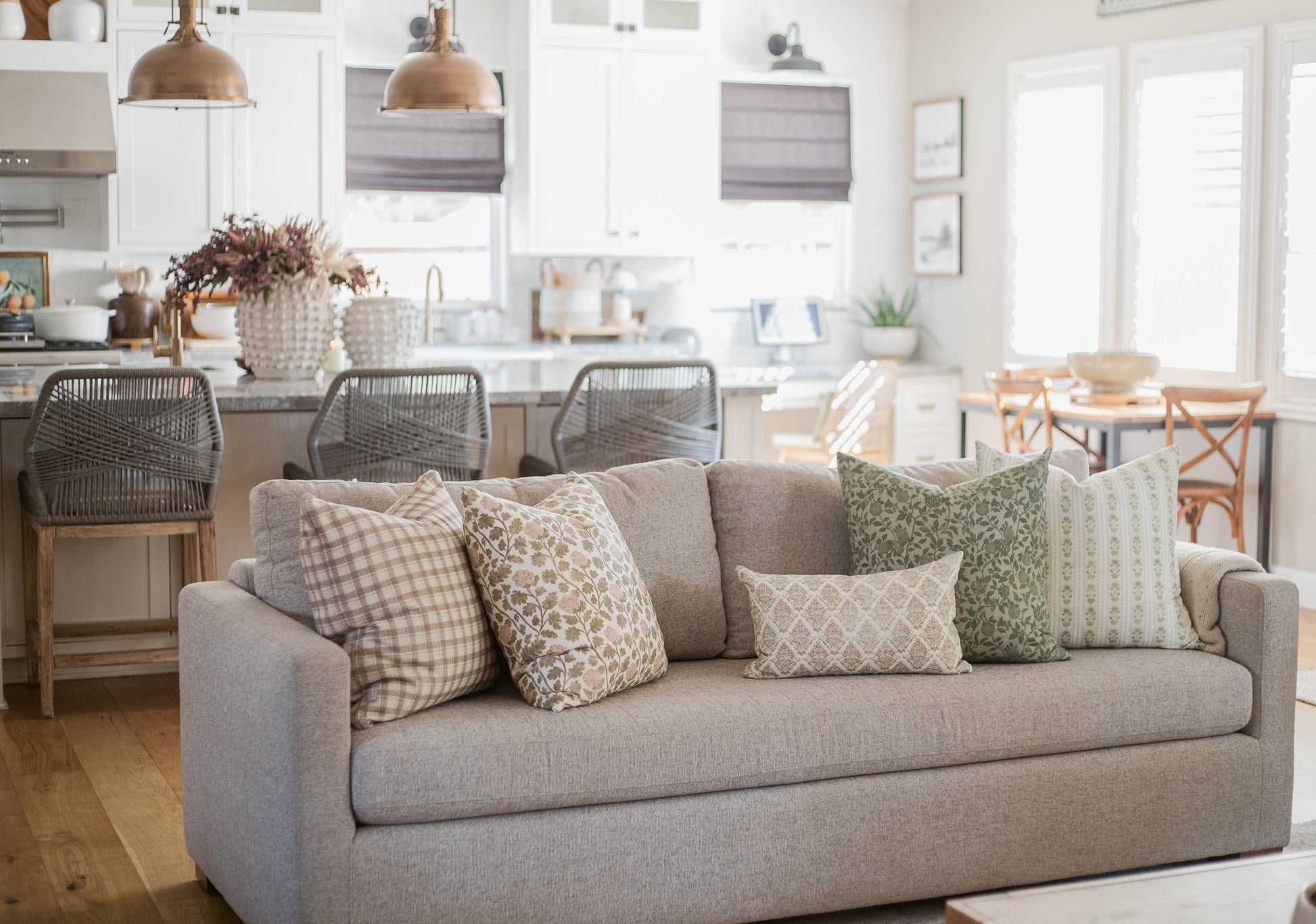 Five throw pillows in various neutral patterns displayed on a beige sofa in a living room setting.