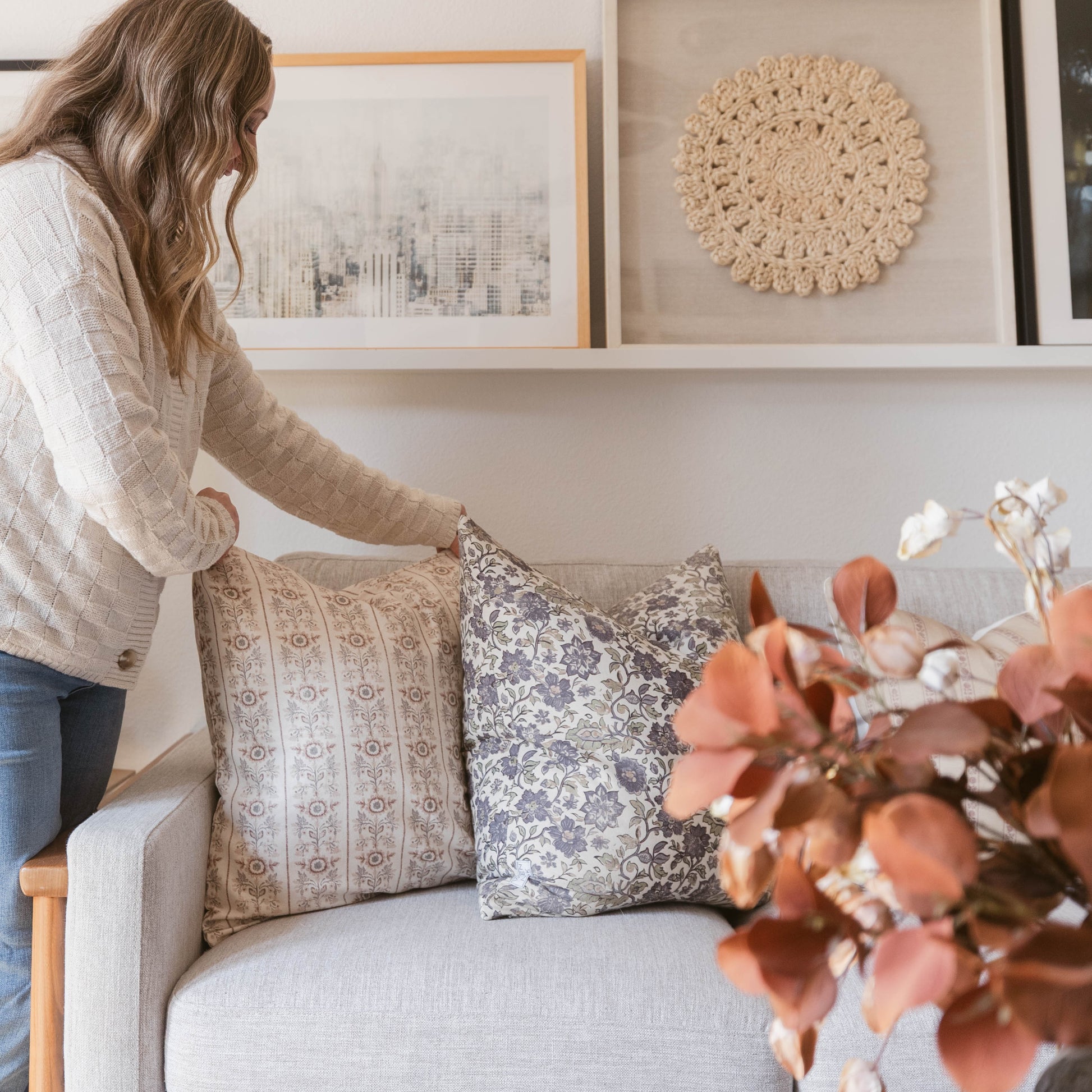 Crocheted round wall hanging in natural cream color displayed on shelf above couch with pillows.