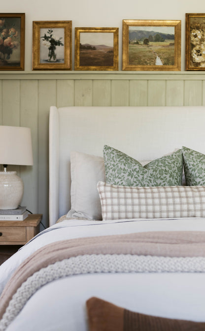 Cream cotton throw pillow with thick weave texture displayed on a bed with green and beige patterned pillows.