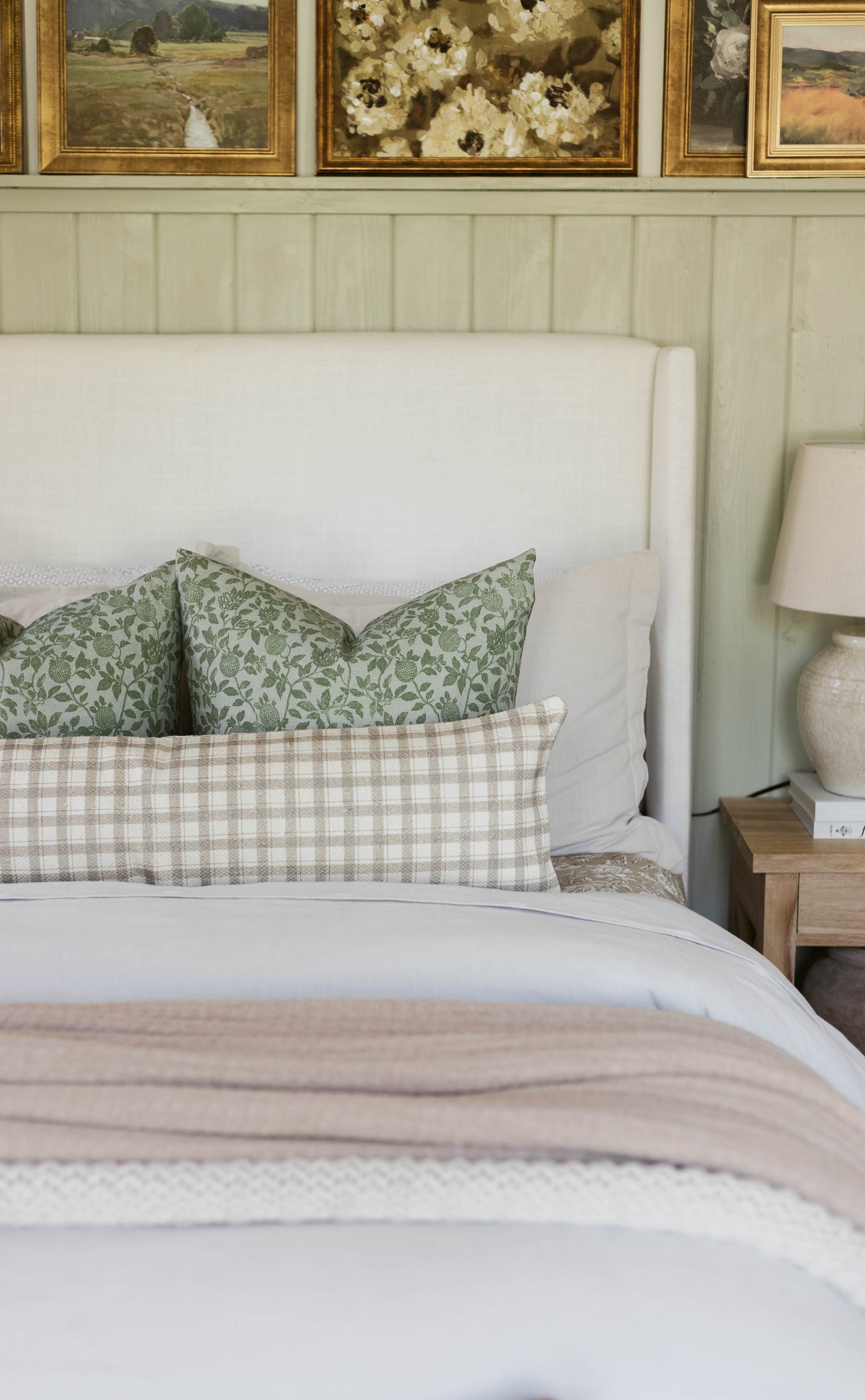 Green floral patterned pillow on a made bed with white headboard and neutral bedding.