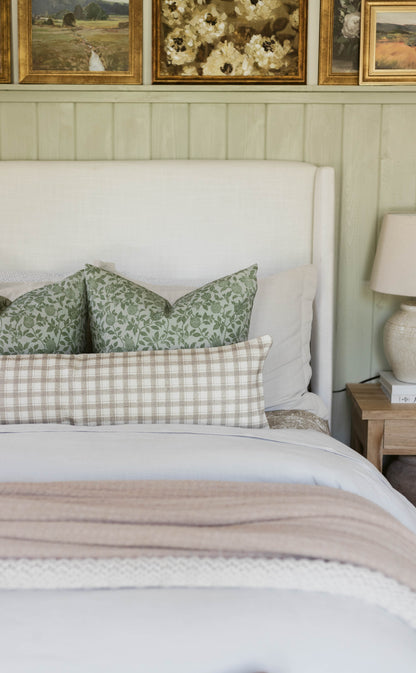 Green floral patterned pillow on a made bed with white headboard and neutral bedding.