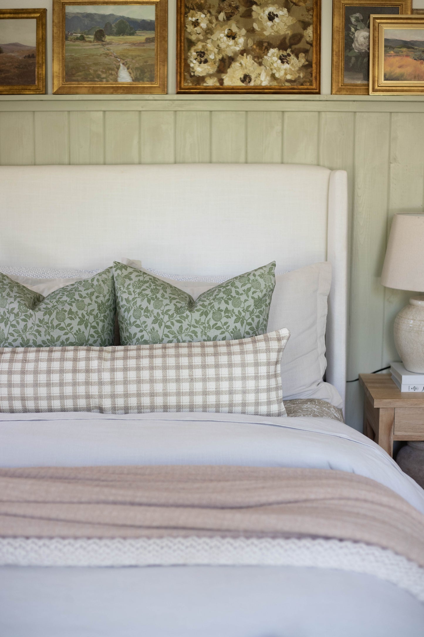 Beige and white gingham cotton lumbar pillow on bed with green patterned pillows and white headboard.