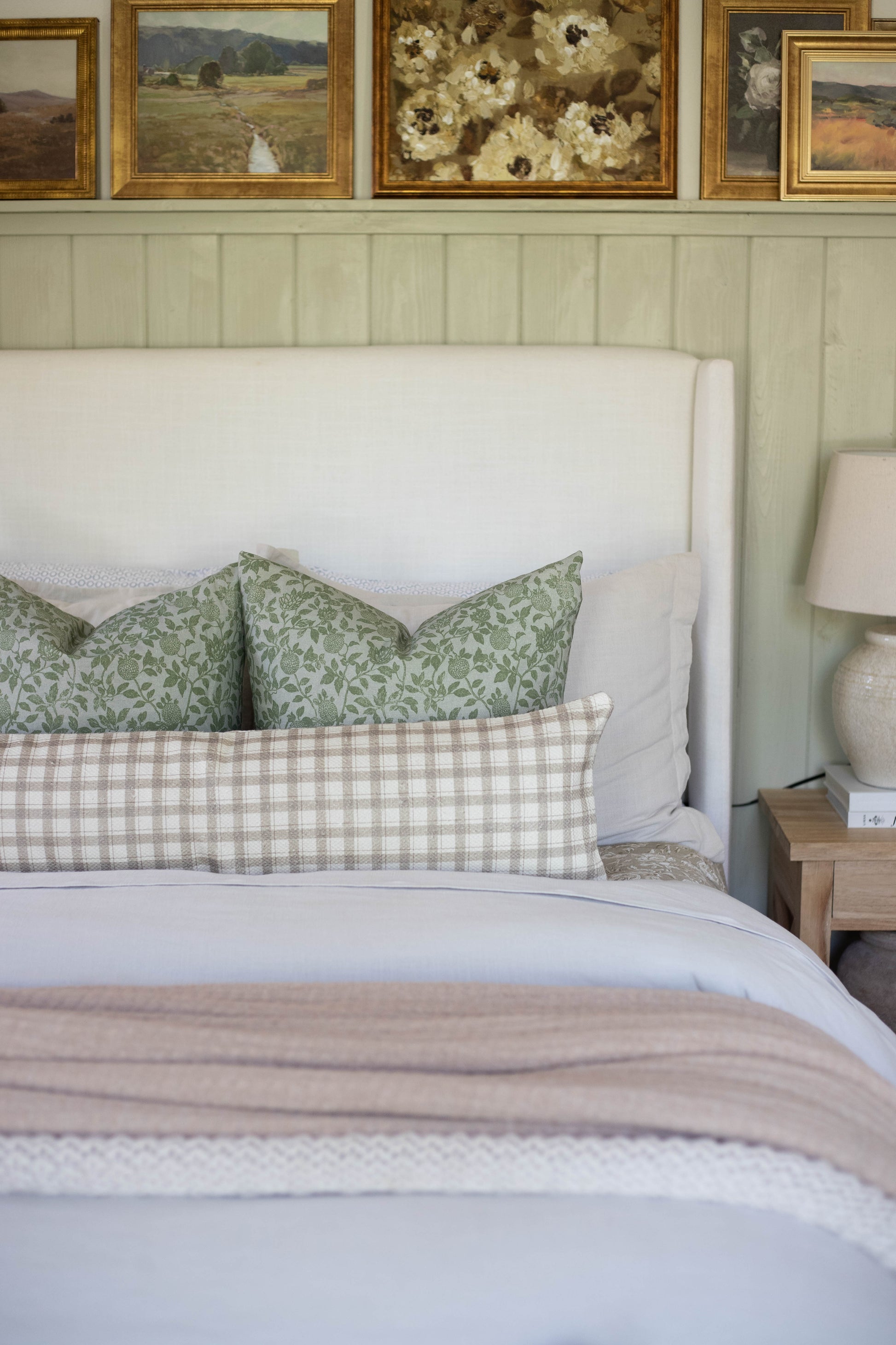 Beige and white gingham cotton lumbar pillow on bed with green patterned pillows and white headboard.