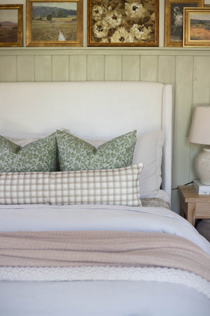 Beige and white gingham cotton lumbar pillow on bed with green patterned pillows and white headboard.