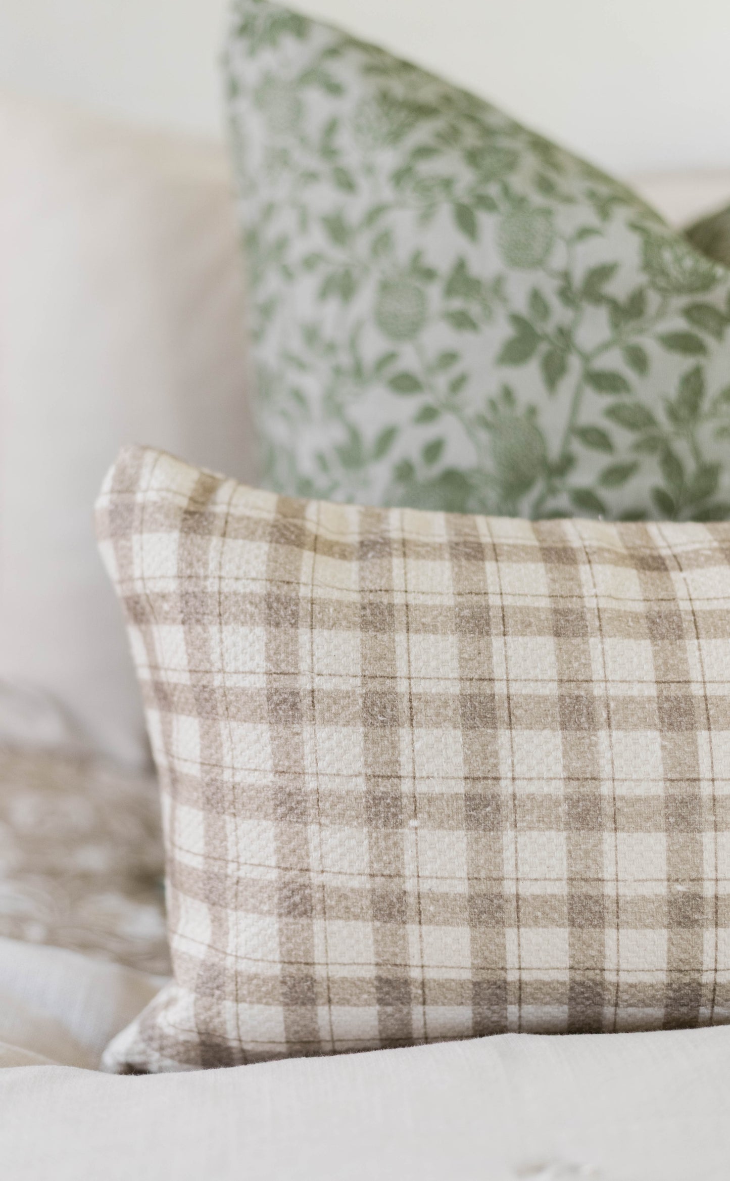 Beige and cream plaid cotton pillow with green botanical patterned pillow in background.