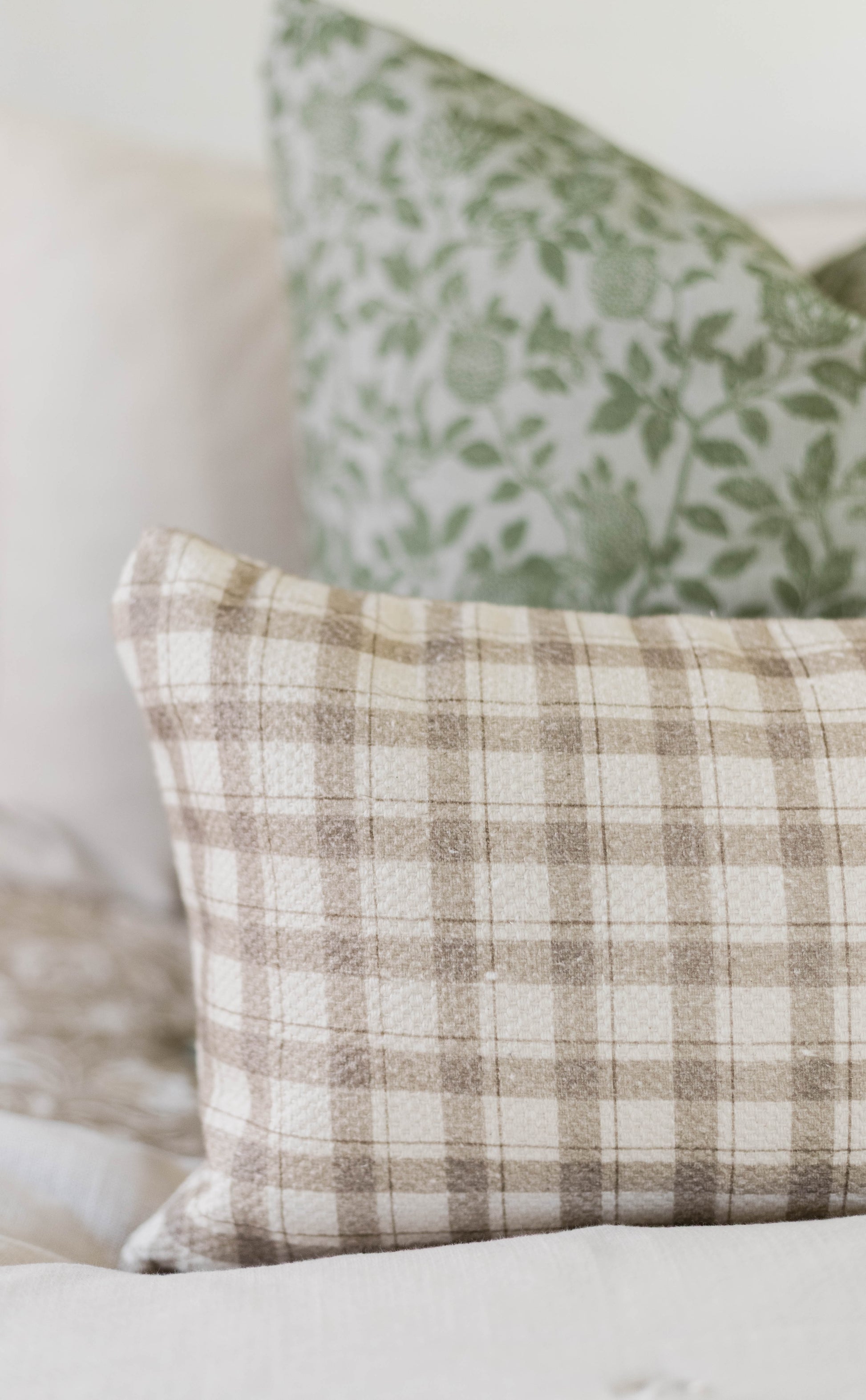 Beige and cream plaid cotton pillow with green botanical patterned pillow in background.