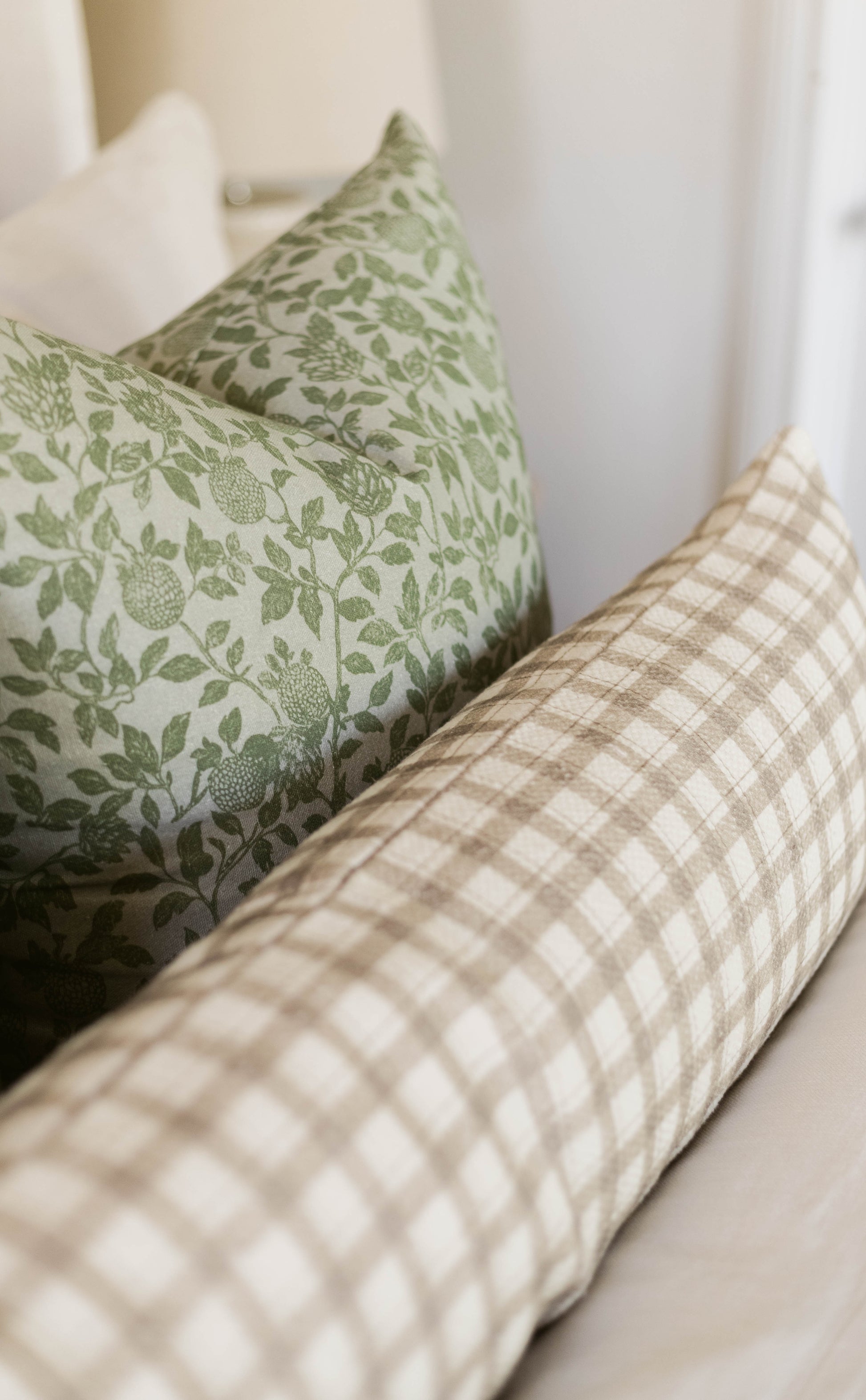 Green and cream botanical patterned pillow with white and beige checkered pillow on neutral background.