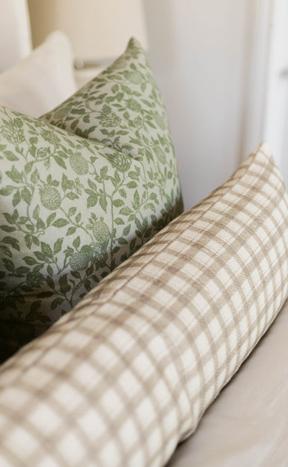 Green and cream botanical patterned pillow with white and beige checkered pillow on neutral background.