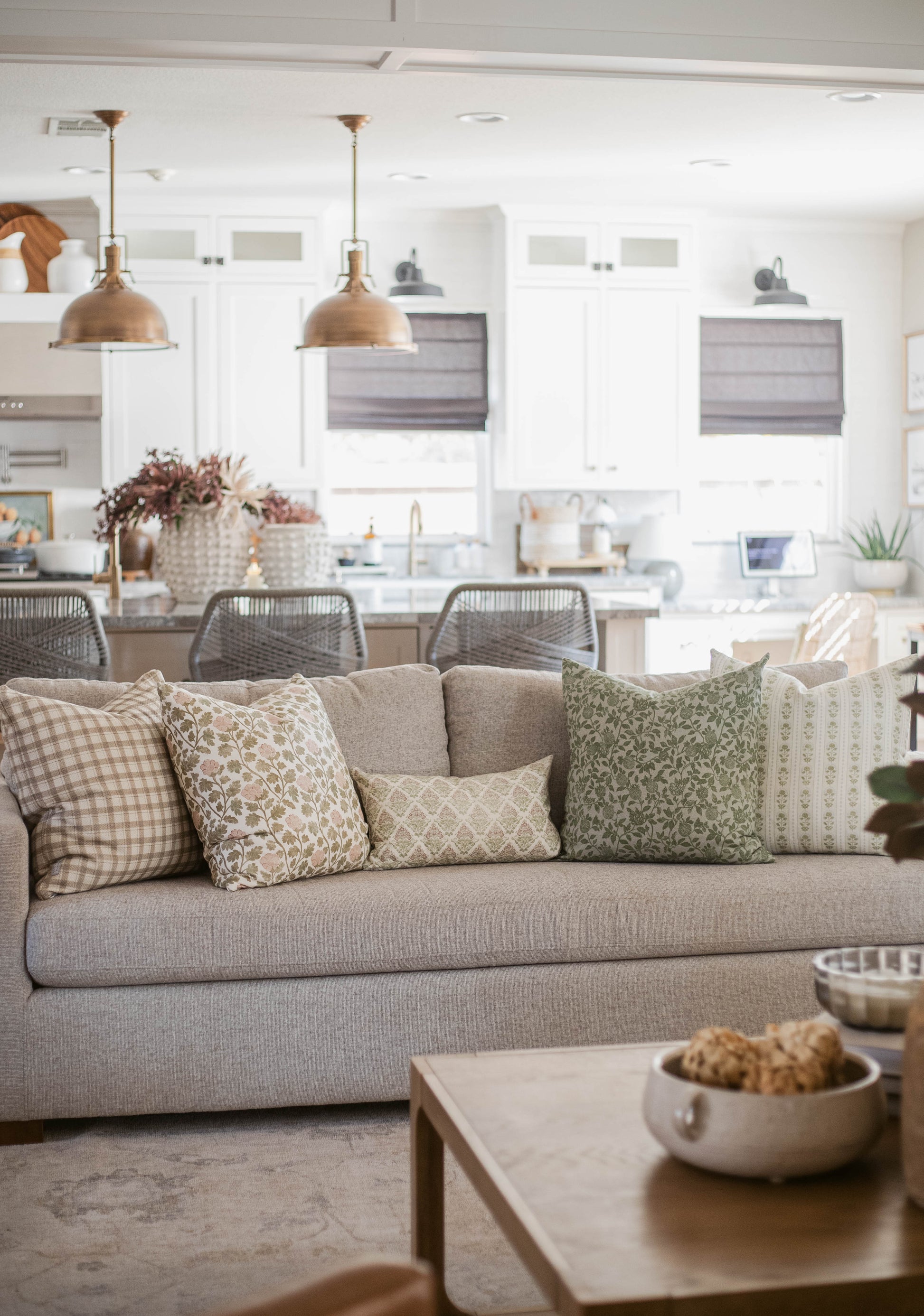Five decorative throw pillows in varying patterns and neutral tones arranged on a beige sofa in a living room setting.