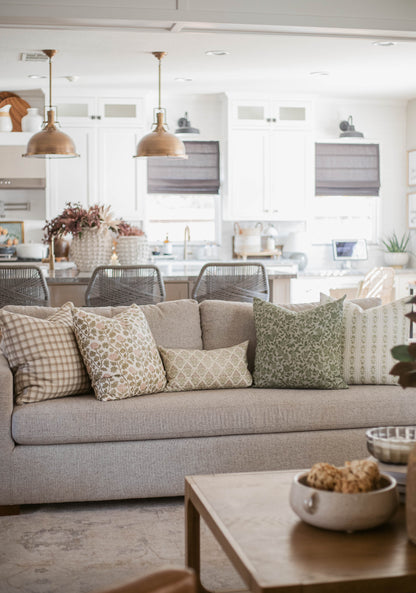 Five decorative throw pillows in varying patterns and neutral tones arranged on a beige sofa in a living room setting.