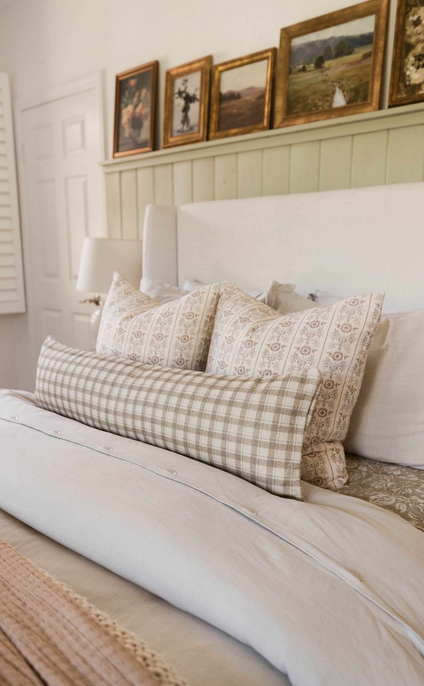 Two decorative pillows with tan geometric and floral patterns arranged on a white bed with matching white headboard.