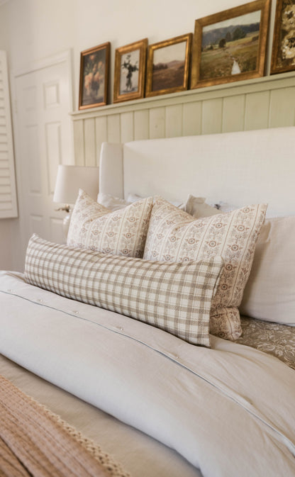 Two decorative pillows with tan geometric and floral patterns arranged on a white bed with matching white headboard.