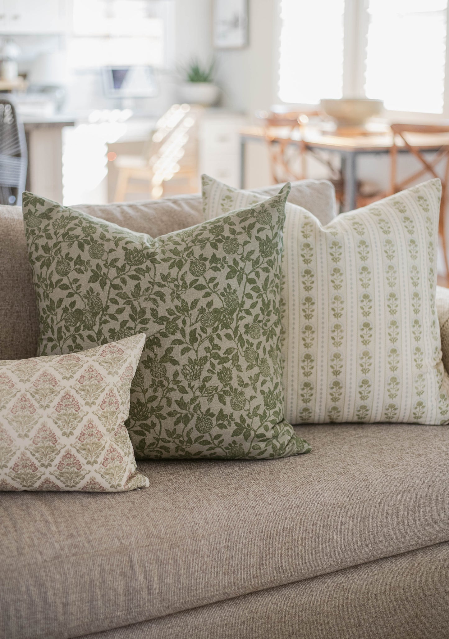 Green and cream patterned throw pillows with floral and striped designs on a gray upholstered sofa.
